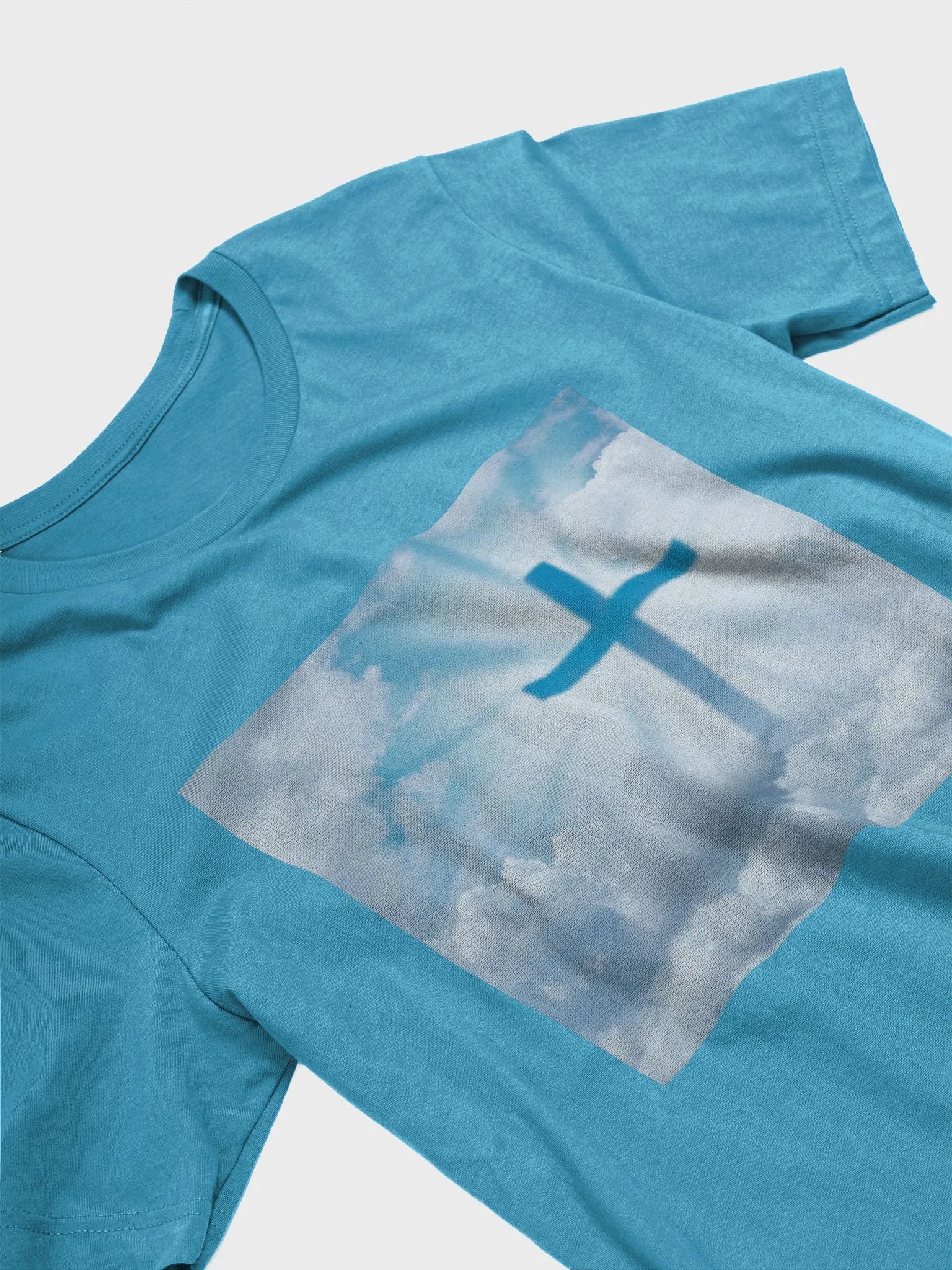 A cross surrounded by a heavenly scene, with rays of light shining through soft clouds in a bright blue sky t-shirt product image (10)