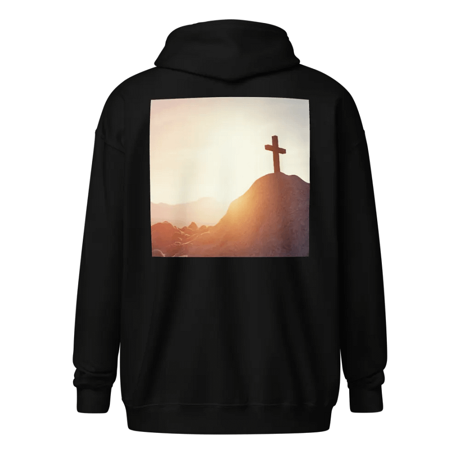 A cross placed on top of a rocky hill, bathed in the warm glow of a sunrise or sunset Hoodie product image (1)