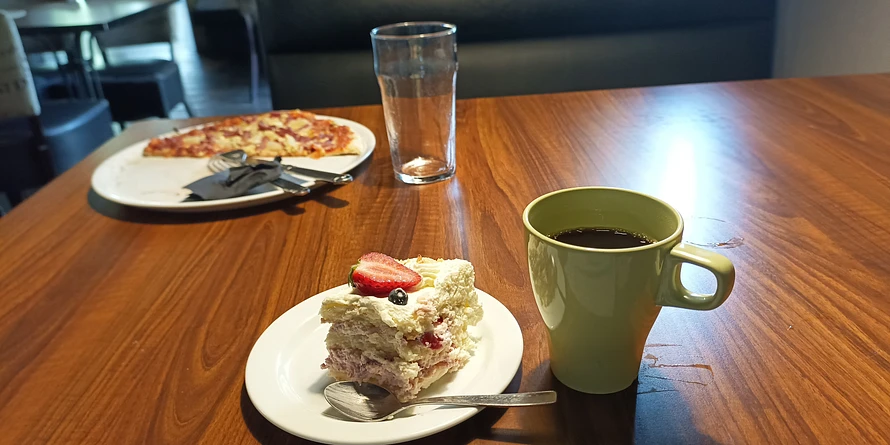A photo of pizza, koffee and cake on a table.