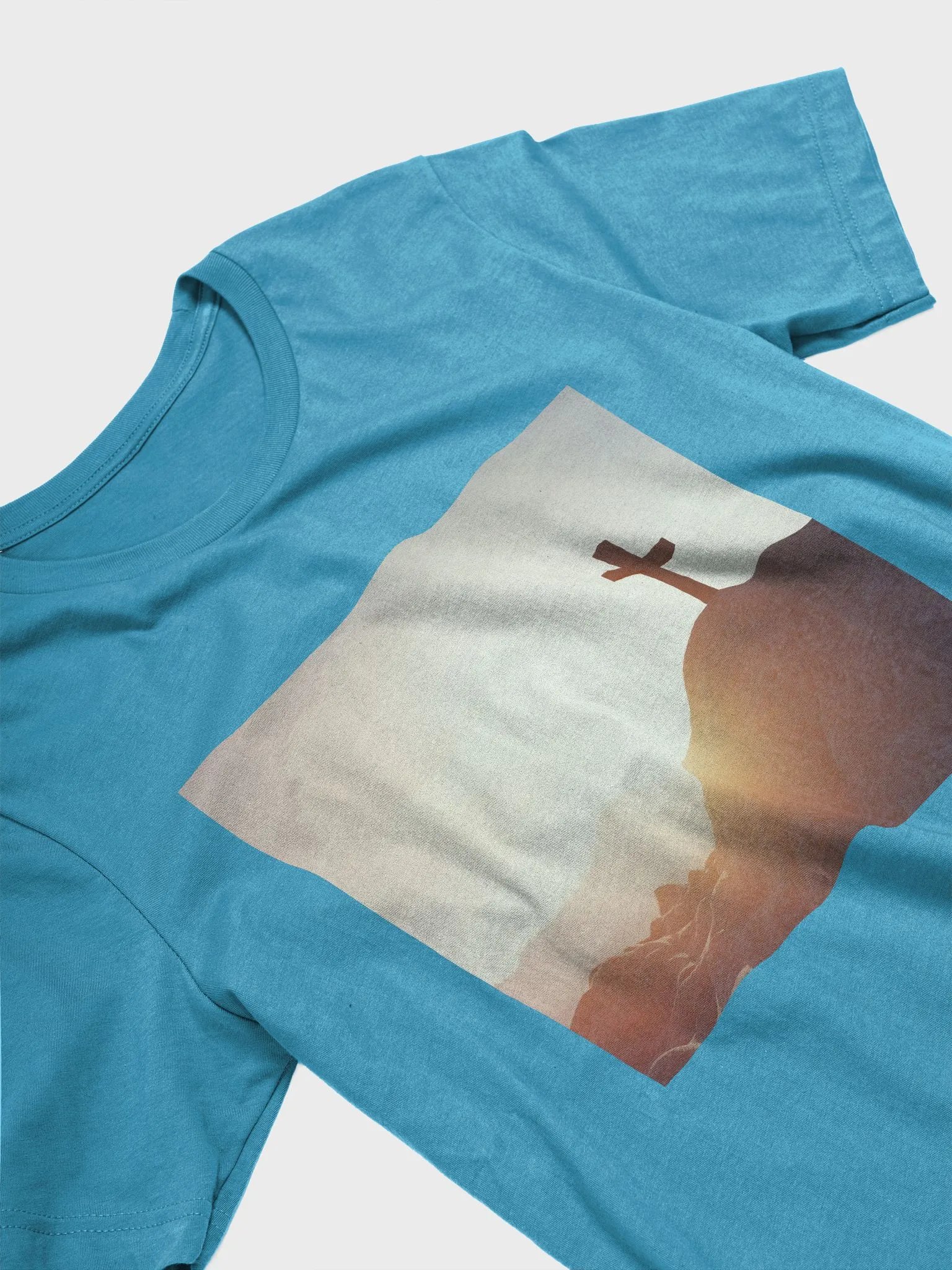 A cross placed on top of a rocky hill, bathed in the warm glow of a sunrise or sunset t-shirt product image (7)