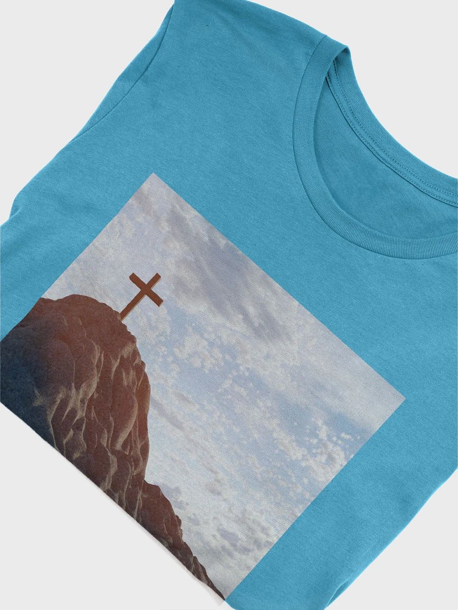 Wooden cross standing atop a rocky hill or mountain, under a sky filled with soft clouds and warm sunlight t-shirt product image (10)