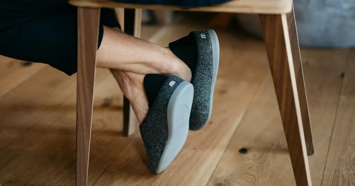 Man wearing supportive indoor shoes while sitting on a chair, showing relaxed feet alignment and natural posture — representing comfort, awareness, and plantar fasciitis recovery through proper footwear.
