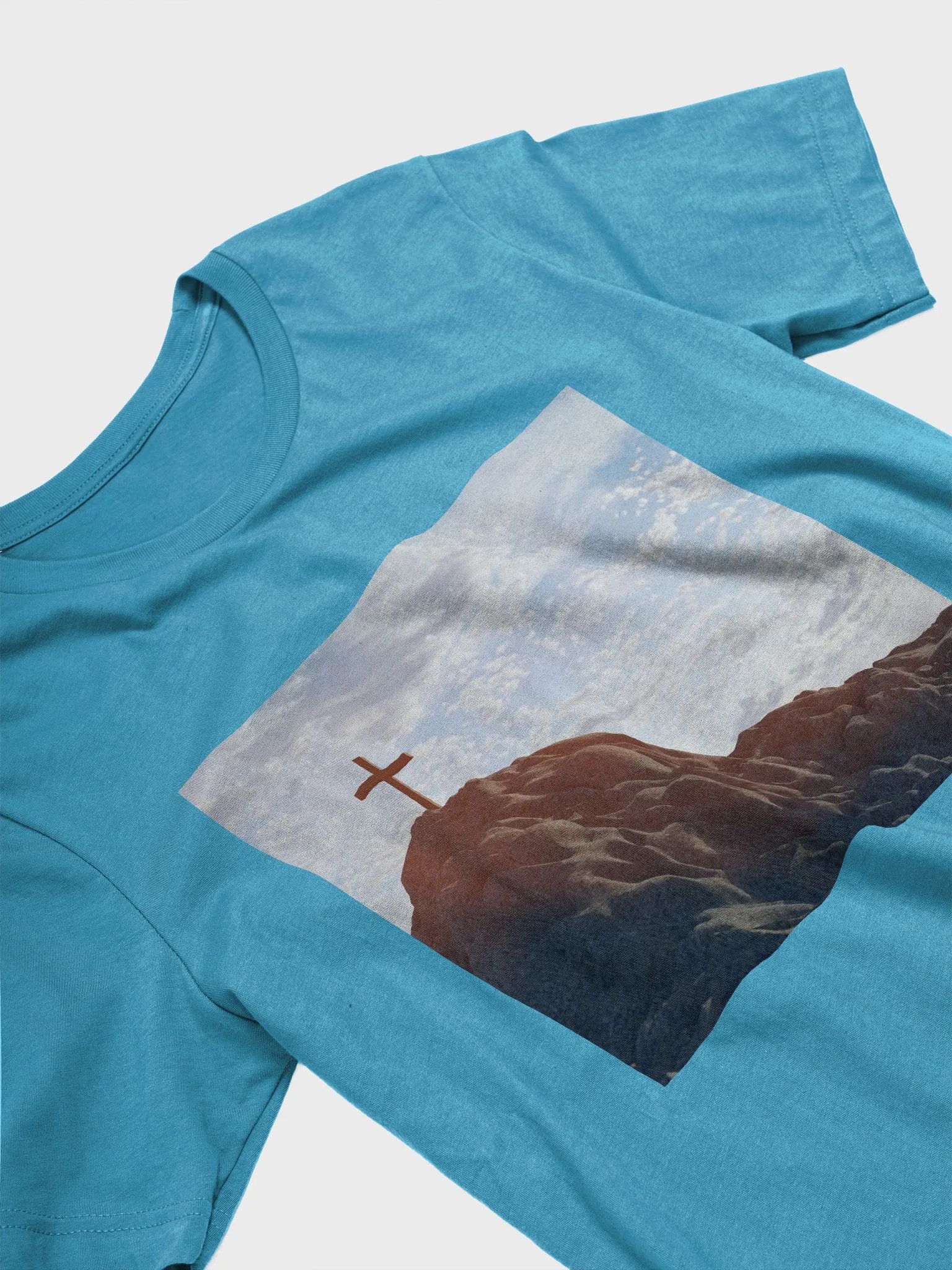Wooden cross standing atop a rocky hill or mountain, under a sky filled with soft clouds and warm sunlight t-shirt product image (9)