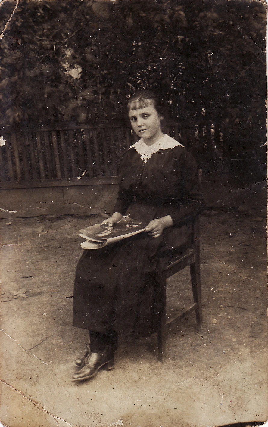 Young woman in a dark dress with a white collar. Her hair pulled back except for a thin fringe of bangs. The photo is in a darkened sepia tone.