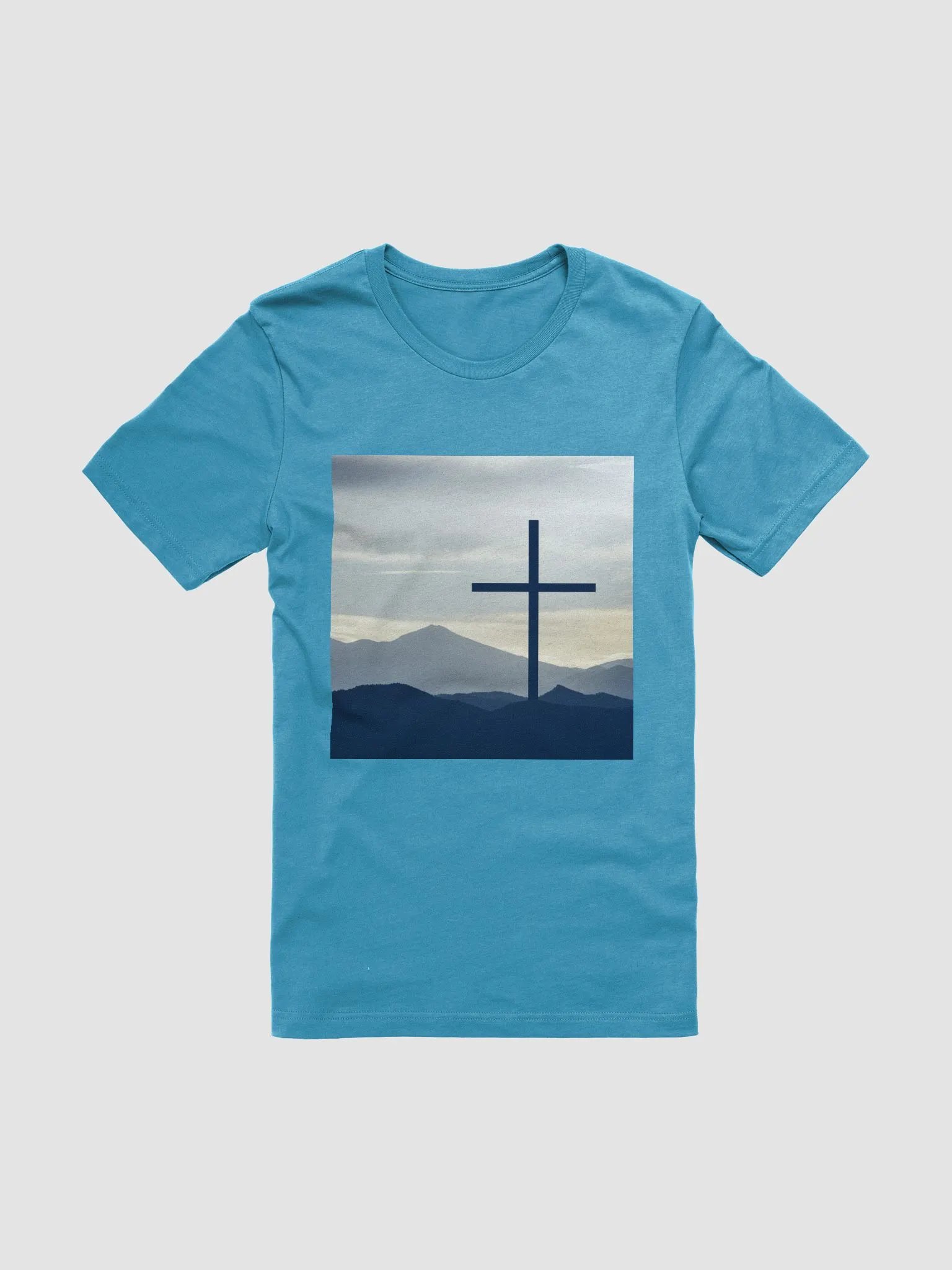 A cross standing against a serene landscape of rolling hills and distant mountains under a soft, cloudy sky t-shirt product image (1)
