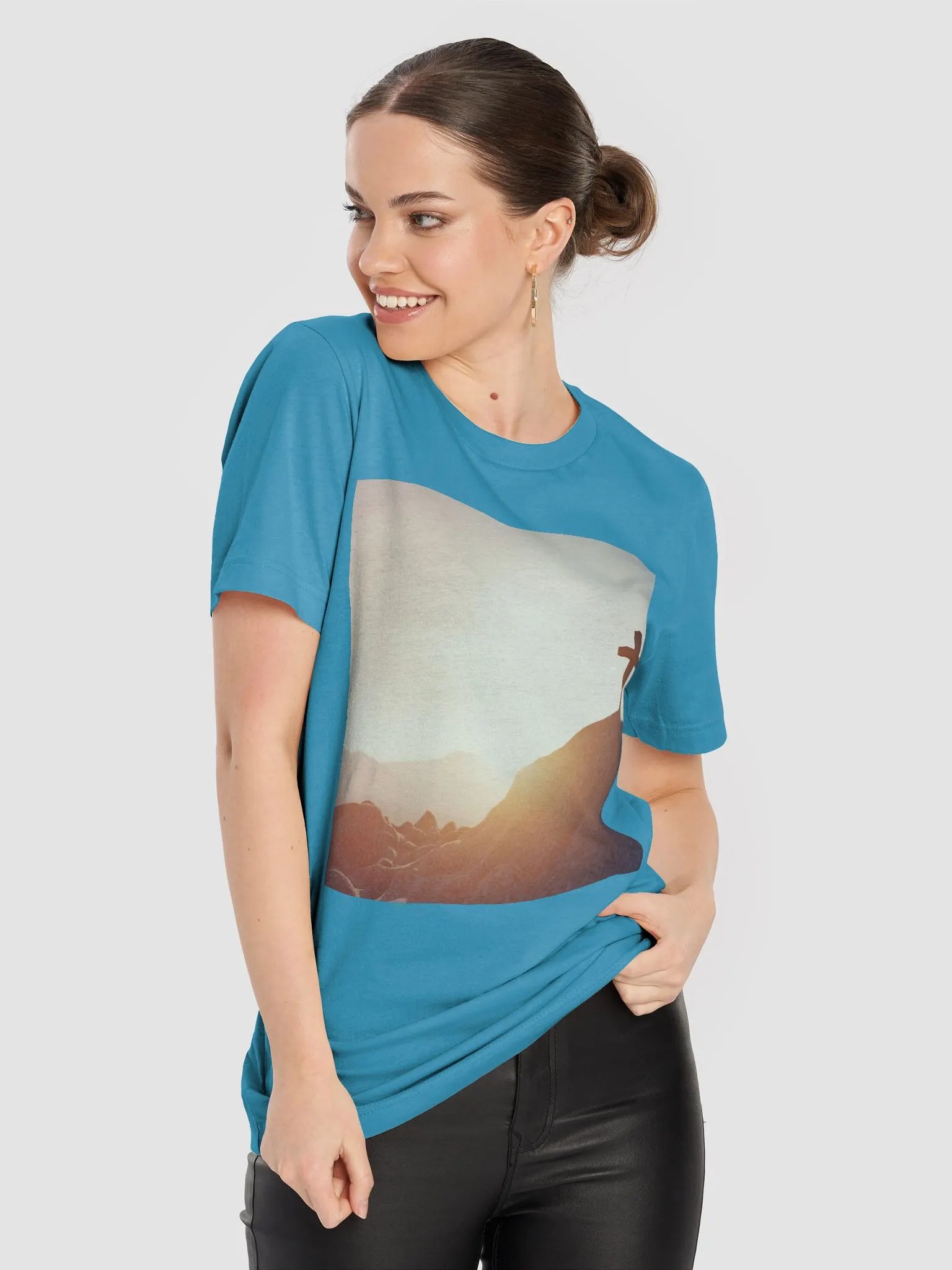 A cross placed on top of a rocky hill, bathed in the warm glow of a sunrise or sunset t-shirt product image (6)