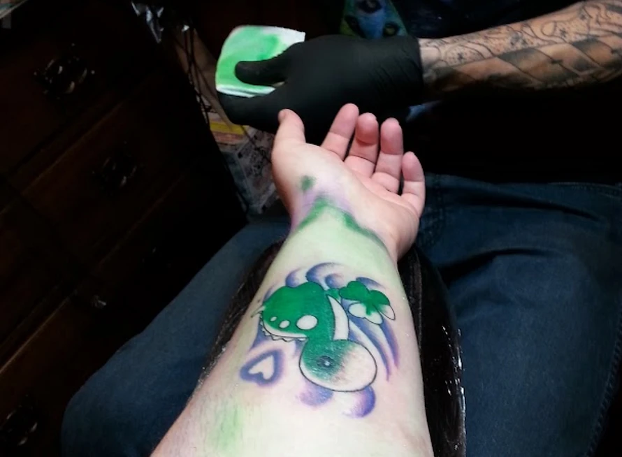 an overturned forearm where a woman is getting a green and purple dinosaur tattoo out of impulsivity