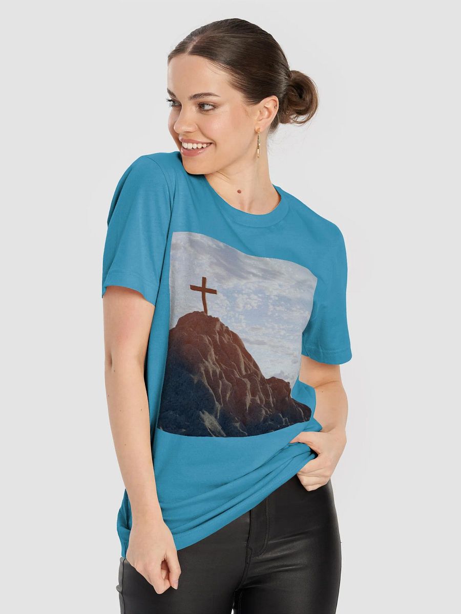 Wooden cross standing atop a rocky hill or mountain, under a sky filled with soft clouds and warm sunlight t-shirt product image (7)