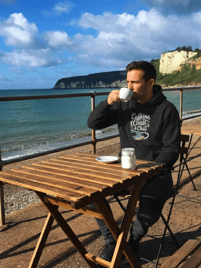 Caffeine, Coast & Chill Hoodie – Your Cozy Cornwall Escape product image (1)