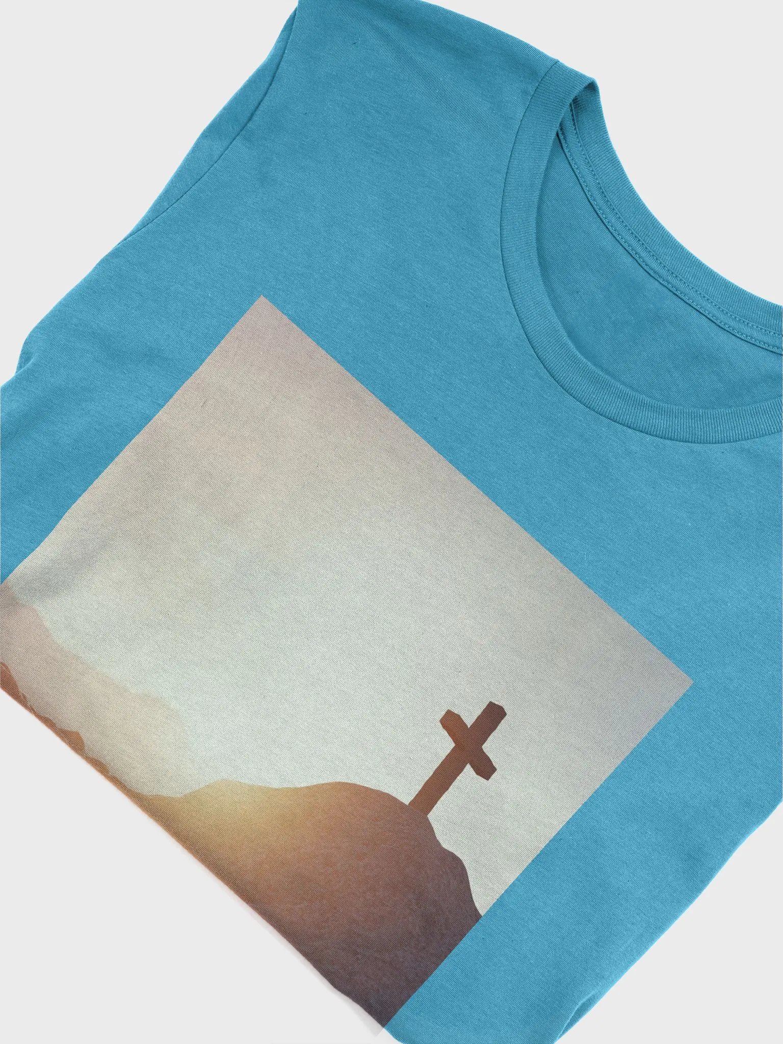 A cross placed on top of a rocky hill, bathed in the warm glow of a sunrise or sunset t-shirt product image (10)