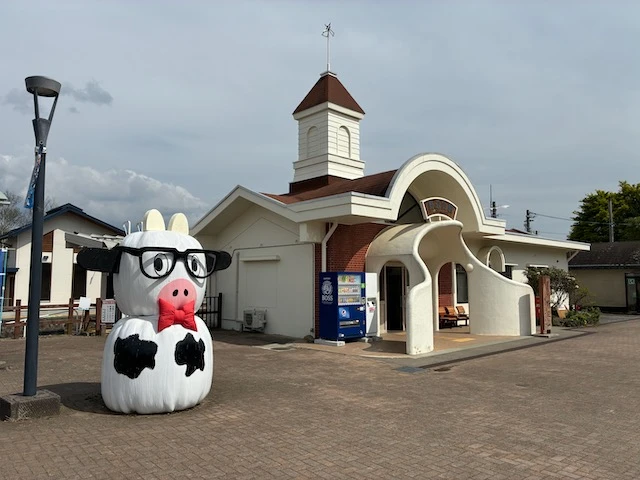 A cute, small train station with a cartoonish statue of a cow.